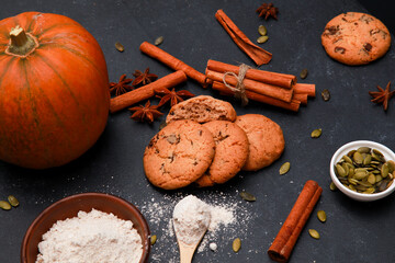 Spices, orange pumpkin, cookies and flour in bowl on black table. Autumn menu or bakery concept. Fall, home baked pastry, thanksgiving, high angle, closeup