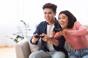Excited Asian Couple Playing Videogames Sitting On Couch At Home © Prostock-studio