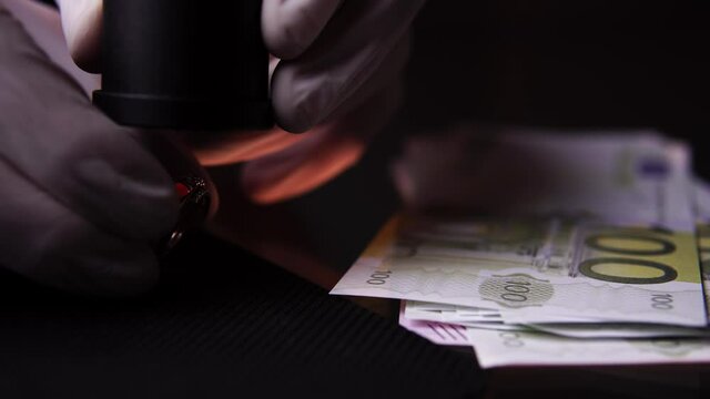 Hands of a pawnshop owner who is appraising gold ring by magnifying glass in close-up. He carefully examines jewel through loupe and takes away money from table. There is buying-up of precious metals.