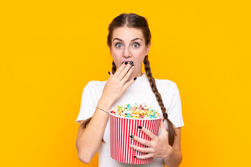 Young woman over isolated yellow background holding a big bucket of popcorns