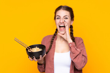 Young woman over isolated yellow background shouting with mouth wide open while holding a bowl of...