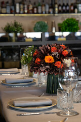 A bouquet of flowers on a cafe or restaurant table served at several guests. Shallow depth of field, blurred background
