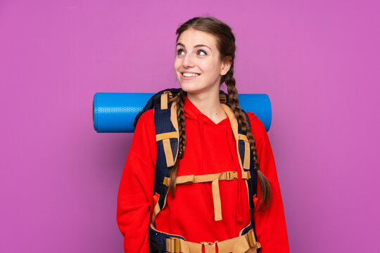 Young mountaineer girl with a big backpack over isolated purple background laughing and looking up