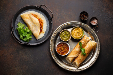 Different types of traditional Indian rice pancakes Dosa. Dosa filled with vegetables sambar and plain Dosa served with dips chutney, on metal plate, stone background. Dish of South India, top view