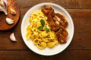 A plate of pasta in a creamy sauce with cheese and chicken on the table next to the garlic board.