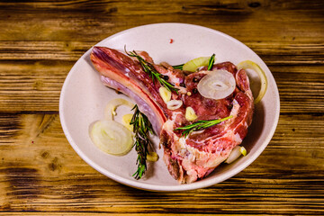 Raw ribeye steak, spices, rosemary, onion and garlic in a ceramic plate on wooden table