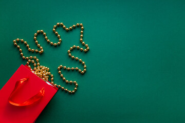 Festive christmas decoration with red gift bag and golden chain over the green background. Christmas and new year concept flatly with space for text.