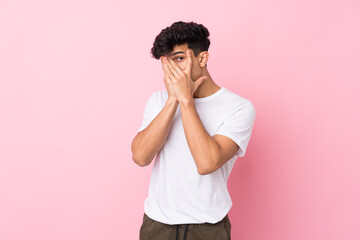 Young Argentinian man over isolated pink background covering eyes and looking through fingers