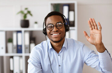 Happy black consultant with headset waving at camera