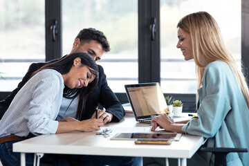 Happy young couple signing bank loan agreement with real-estate agent to buying the house in the office.