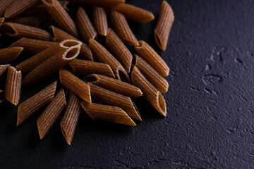 Wholegrain pasta, macaroni pasta on dark background. Top view.