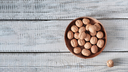 On a wooden background, a wooden plate filled with walnuts.