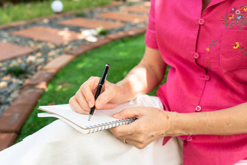 senior retired woman writing diary and sitting in backyard at home