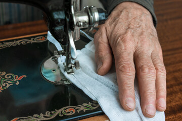 wrinkled hand of older man sewing protective facemask in lockdown time