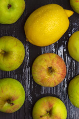 Ripe lemon and fresh village apples on a wet wooden background
