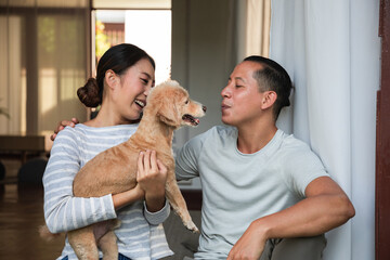 Diversity young couple Play with his dog in the house. They are hugging their little puppy