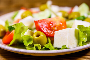 Ceramic plate with greek salad on wooden table