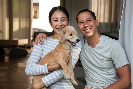 A portrait of a young Asian couple and their dogs photographed together in the house. They smile and look at the camera.