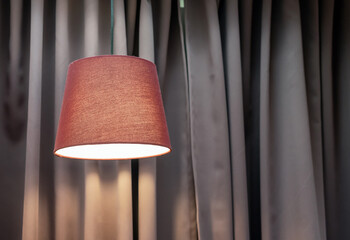 Lamp with a brown fabric lampshade against a background of beige curtains.