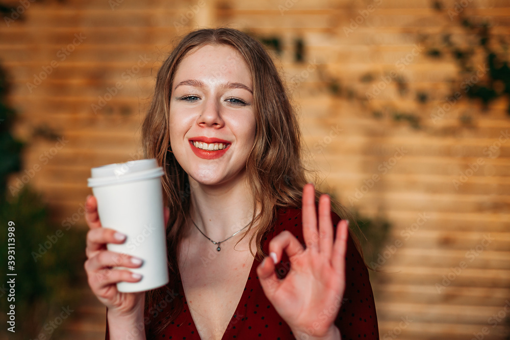 Wall mural young beautiful woman with blue eyes drinking cup of takeaway coffee with happy face smiling doing o