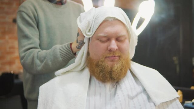 Hairdresser dabs the head of a bearded man with a&nbsp;towel.