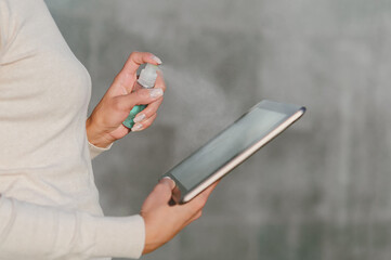 Closeup, Disinfects the tablet with Antiseptic. Against the background of a gray concrete wall.