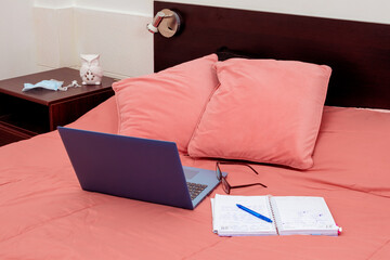 Open laptop, diary and glasses on a bed in a bedroom. I work from home, comfortable form of communication or entertainment. Current concept of work from home.