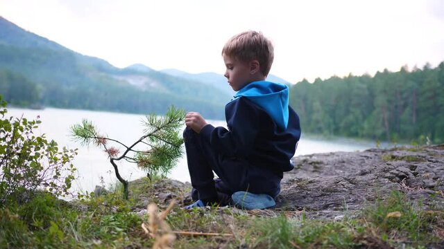 A child is sitting on the riverbank on a cliff. Evening time