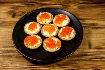 Tartlets with red caviar and soft cheese on a wooden table