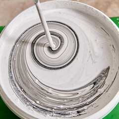 Worker is making new color with mixer in basket for painting walls.