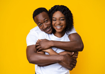 Loving black couple cuddling on yellow background