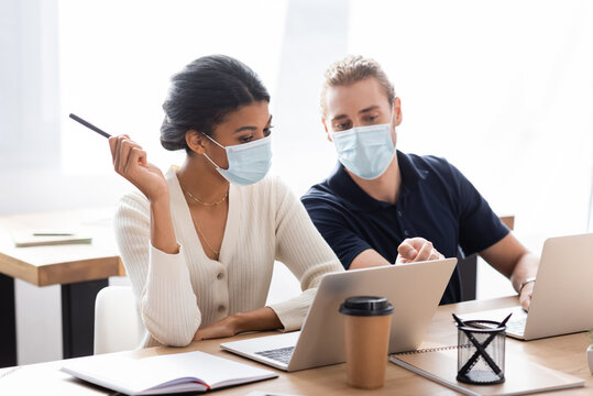 young afrcan american businesswoman with colleague in medical mask discussing project near laptop