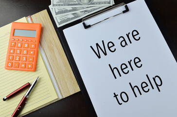 Top view of banknotes, notebook, calculator, pen, paper holding file and white paper written with text WE ARE HERE TO HELP. Business and education concept. 