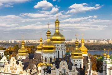 Fototapeta na wymiar Beautiful yellow and gold domes of the Orthodox Church against the background of the blue sky and the city. Domes of the Assumption Cathedral of the Kiev-Pechersk Lavra.