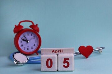 April 5st. White wooden calendar blocks with date, clock and stethoscope on a blue pastel...
