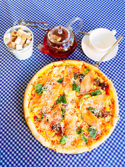 Freshly baked pizza with a teapot, a cup and a bowl of sugar stands on a checkered table. Top view
