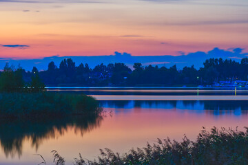 Sunset over a calm lake Pogoria III with shadows, colorful sky and trees in background.