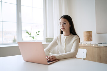 Cute teenager girl sitting at table and doing homework. Education concept, distance learning, self-education, video conference class with tutor    