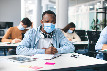 Black male student in mask sitting at desk in classroom