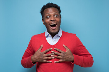 Astonished afro american guy being surprised receiving compliment. Studio shot on blue wall.