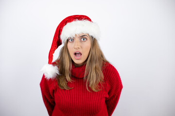 Young pretty blonde woman wearing a red casual sweater and a christmas hat over white background afraid and shocked with surprise and amazed expression, fear and excited face.
