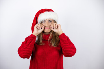 Young pretty blonde woman wearing a red casual sweater and a christmas hat over white background depressed and worry for distress, crying angry and afraid. Sad expression.