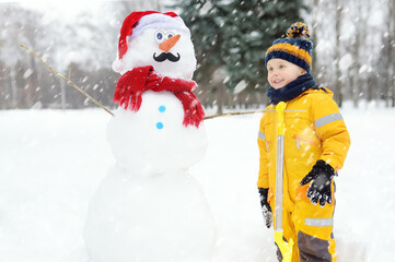 Fototapeta na wymiar Little boy playing with funny snowman. Active outdoors leisure with children in winter.