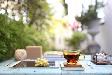 Transparent tea cup and tablet with books on blue wooden table at outdoor
