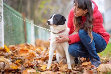 A dark-haired girl in a red jacket plays with a dog in an autumn park.