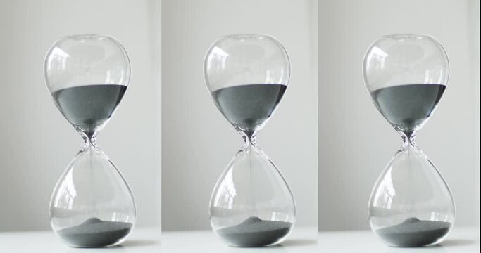 Gray sand running through the hourglass. transparent glass hourglass on the background of a white bedside table. Vertical video, 4k
