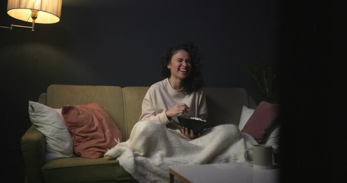 The girl is watching a comedy on TV. To watch series. The girl on the couch with popcorn is watching a movie. 4k slow motion video