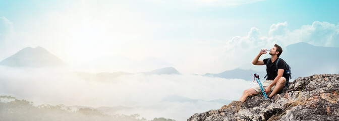 Hiker sitting on top of the mountain and drinking bottled water. Relaxation emotion, banner size.