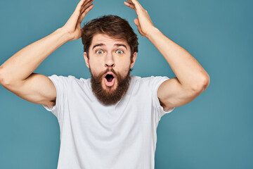 Fototapeta na wymiar A bearded man in a white T-shirt gestures with his hands emotions blue background