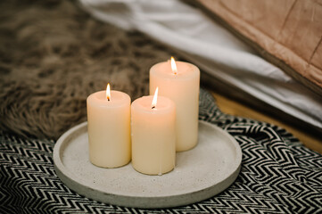 Decor with candles. Still life home atmosphere in the interior with a candles, on the background of cozy bedspreads, the concept of comfort and coziness. Winter elements of home decor. Close up.